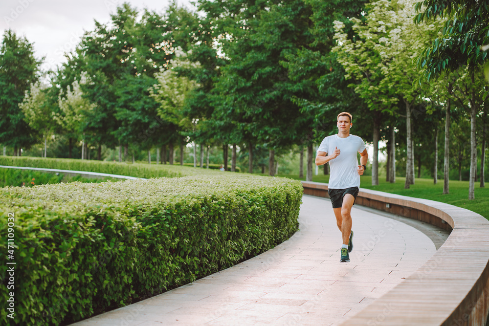 Attractive young man athlete wearing sportswear run in modern park at summer morning. Morning jogging, cardio, weight loss