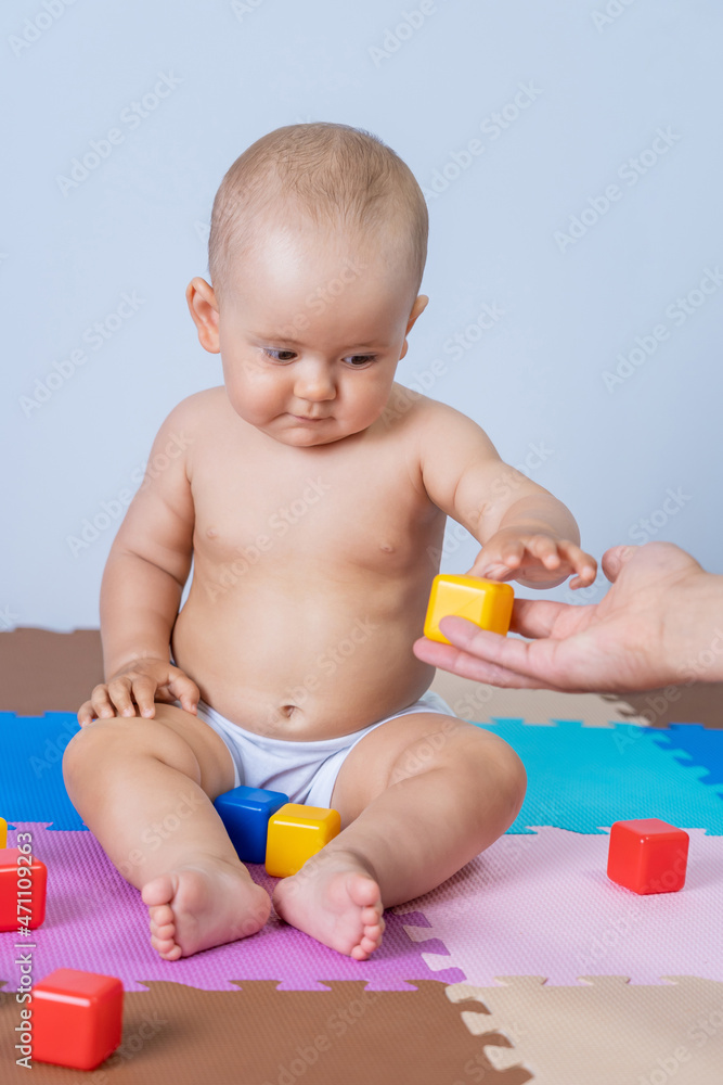 father's hand holds out a toy, a yellow plastic cube to a newborn baby of 8-10 months father's hand holds out a toy, a yellow plastic cube to a newborn baby of 8-10 months