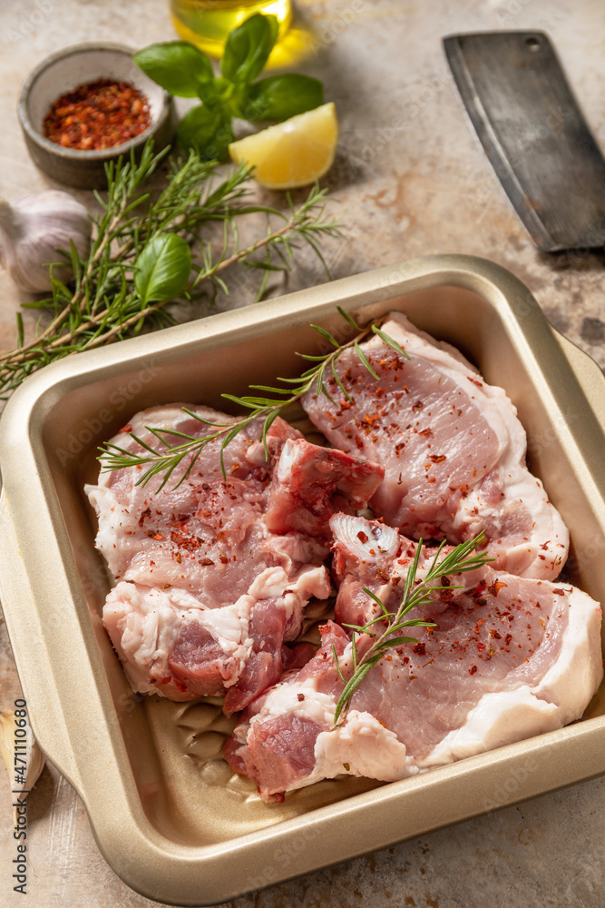 Fresh raw pork loin on the bone with spices and marinade on a stone tabletop, preparation for baking or barbecue. Fresh raw pork loin on the bone with spices and marinade on a stone tabletop, preparation for baking or barbecue.