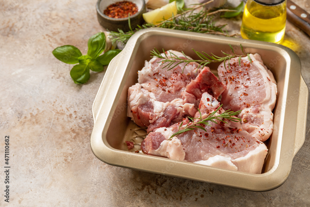 Fresh raw pork loin on the bone with spices and marinade on a stone tabletop, preparation for baking or barbecue. Copy space.