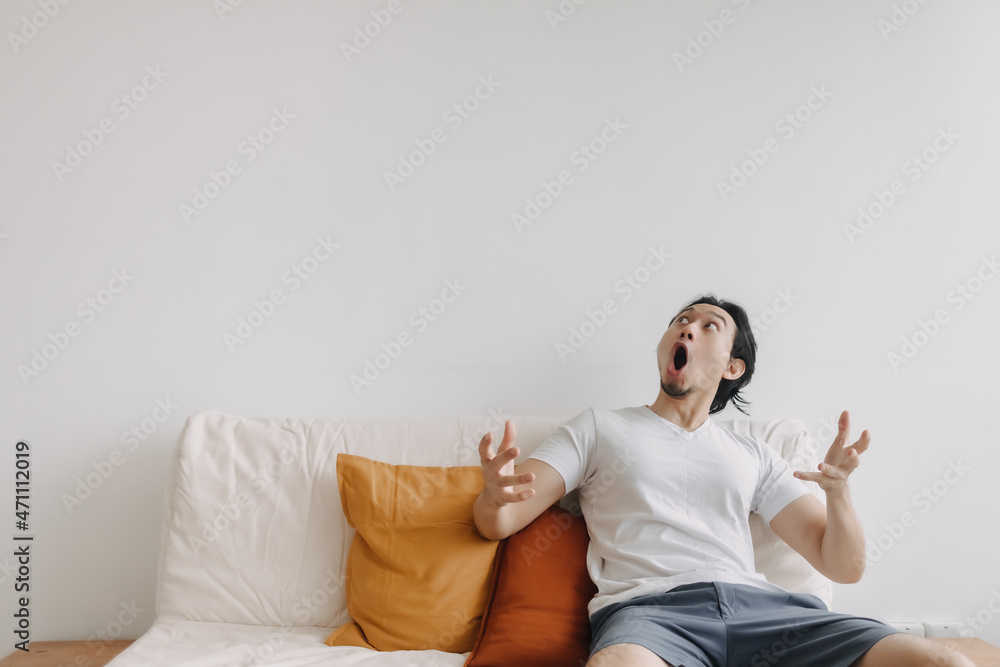 Asian man feels surprised and shocked at empty copy space wall in living room.
