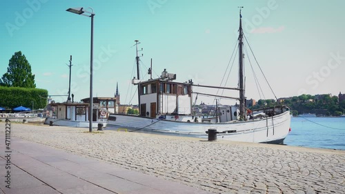 Small old fishing ship at the pier of the city embankment of Stockholm. The ship sways on the waves at the city pavement. Wooden fishing seiner is moored at the Stockholm waterfront. Summer blue sky.