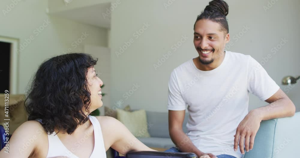 Happy biracial woman in wheelchair and male partner looking at each other and smiling in living room Happy biracial woman in wheelchair and male partner looking at each other and smiling in living room