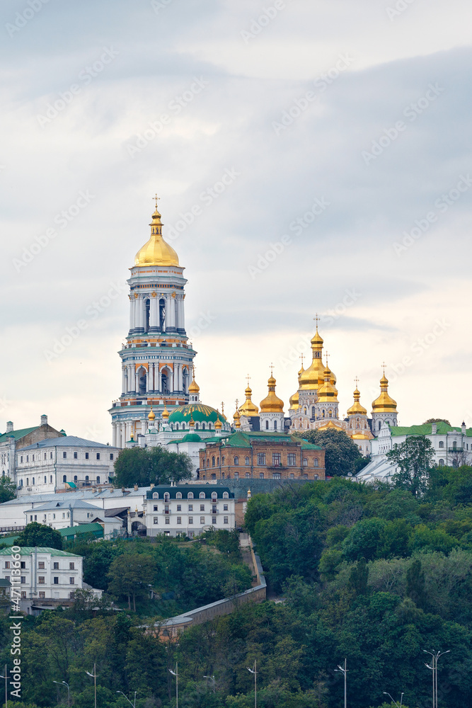 The bell tower of the Pechersk Lavra and the golden domes of the monastery on the slopes of the Kyiv hills on a cloudy summer day. The bell tower of the Pechersk Lavra and the golden domes of the monastery on the slopes of the Kyiv hills on a cloudy summer day.