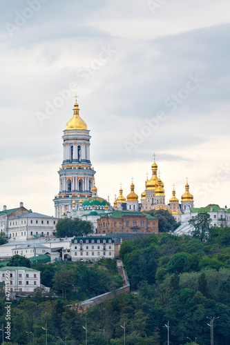 The bell tower of the Pechersk Lavra and the golden domes of the monastery on the slopes of the Kyiv hills on a cloudy summer day.