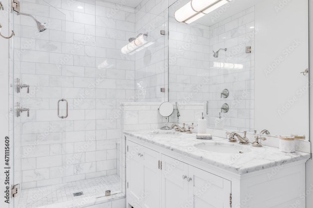 A luxurious white bathroom with a double vanity and bronze faucets, a white subway tile shower, and glass door. A luxurious white bathroom with a double vanity and bronze faucets, a white subway tile shower, and glass door.
