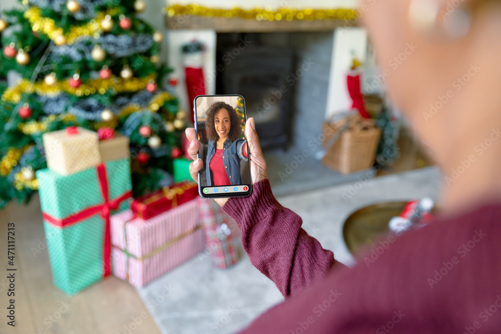 Woman making smartphone christmas video call with smiling african american woman