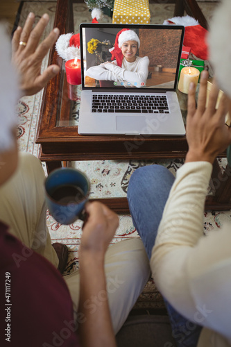 Two waving men making laptop christmas video call with smiling caucasian woman in santa hat