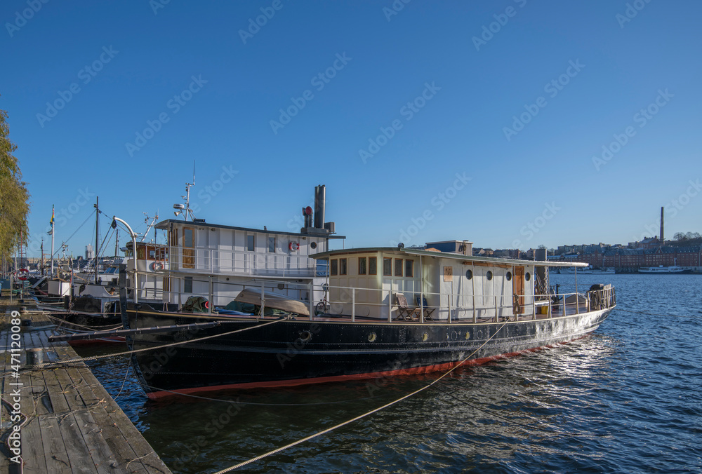 Obraz premium Various boats at the pier Norrmälarstrand at the bay Riddarfjärden in the district Kungsholmen, the tower of the Town City Hall a sunny color full autumn day in Stockholm