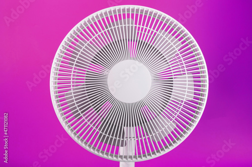 White modern electric fan for cooling the room on a pink background.