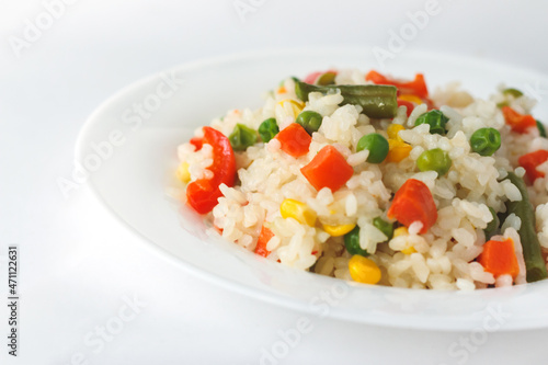 Cooked white rice mixed with colorful vegetables (onion, carrot, green peas, corn, green beans) in white plate.