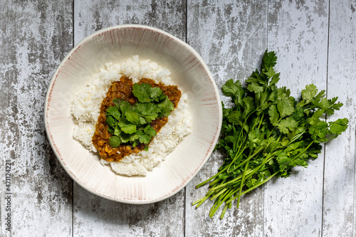 A High Angle View of a Bowl of Dahl and a Bunch of Coriander, on a Table