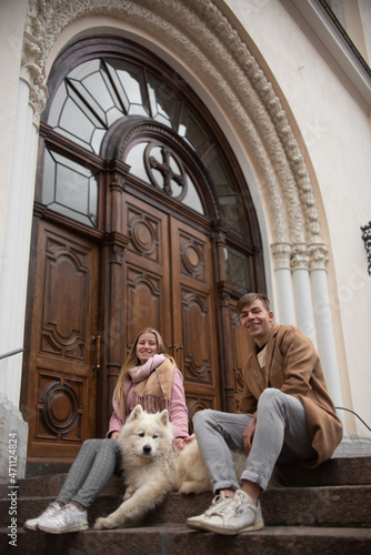 a couple in love a guy and a girl are walking in the parks of a beautiful city in autumn in November with a friend of a white fluffy big dog
