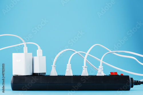 A black mains filter with electrical outlets inserted into it with white plugs of electrical appliances on a blue background