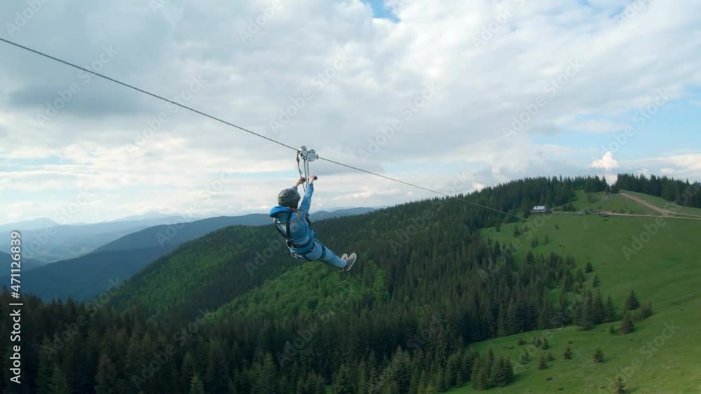 Unusual view of a woman riding a zip line among the mountains. Fast and maneuverable flight around a person. Filmed on FPV drone.