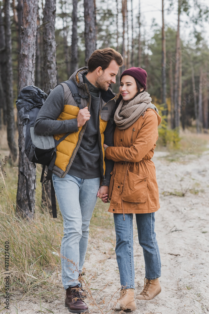 happy young couple in autumn outfit hiking in forest