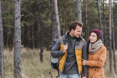 positive young couple talking while walking in autumn clothes in forest