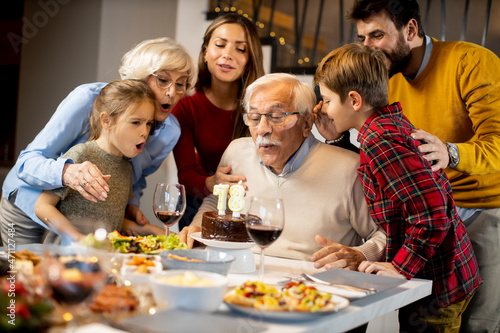 Family celebrating grandfather birthday with cake and candles at home