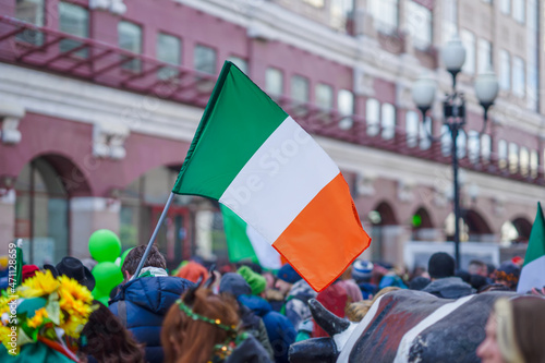 National Flag of Ireland close-up in the hands of man, crowd people, city street during celebration of St. Patrick's Day
