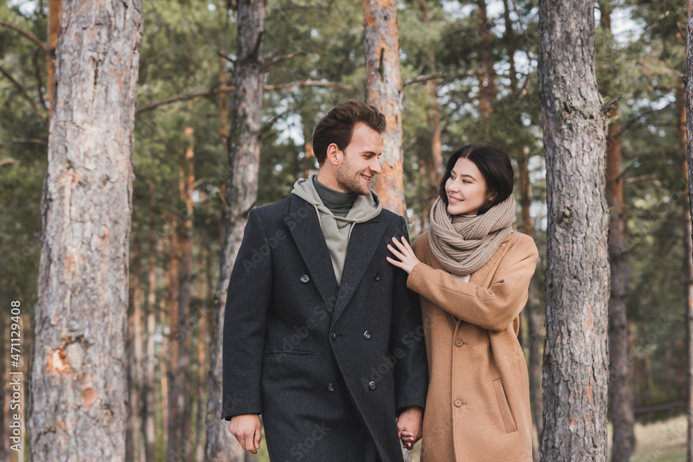 cheerful woman touching shoulder of smiling boyfriend while walking in autumn park cheerful woman touching shoulder of smiling boyfriend while walking in autumn park