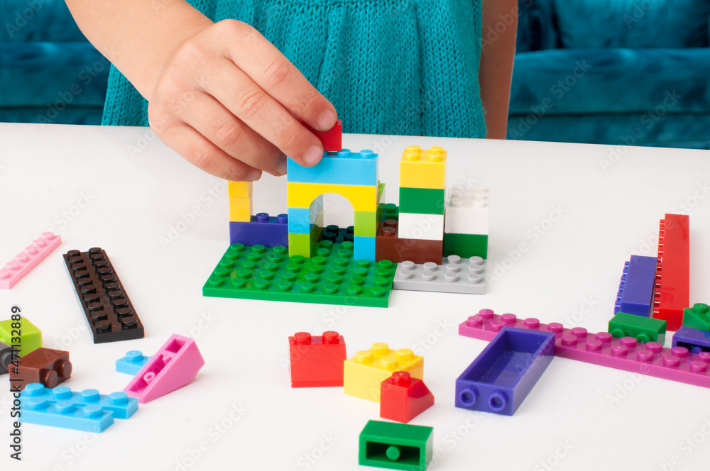Fototapeta premium The child's hand holds a part of a colored plastic construction kit and puts it in its place.