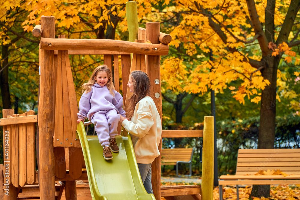 Mom and daughter on playground in autumn. family play on wooden slide. New home babysitter. park for happy family. woman and girl are smile. look at camera. Have fun weekend together. sisters joke