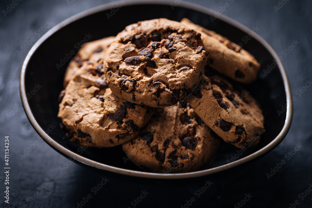 Chocolate chip cookies with tea in background in a dark moody atmosphere Chocolate chip cookies with tea in background in a dark moody atmosphere