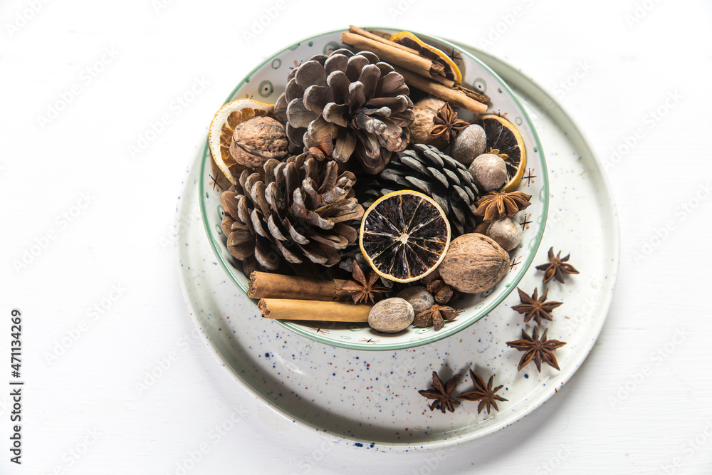 Christmas composition in a bowl. Cones, nutmeg, cinnamon, dried orange slices, anise, walnuts on a tray as home decoration for the New Year on the white wooden table