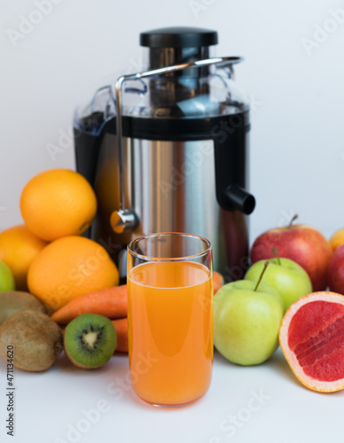 A glass of fresh fruit juice, fruits and a modern juicer extractor on the table. Healthy fruit and vegetable juices at home. Selective focus. Close-up.