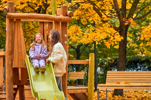 Mom and daughter on playground in autumn. family play on wooden slide. New home babysitter. park for happy family. woman and girl are smile. look at camera. Have fun weekend together. sisters joke