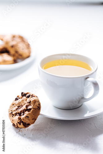 Cup of tea in white cup with chocolate chip cookies as a part of a scene, on a white background