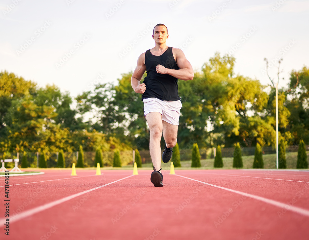 Young muscular fit male sprinter running on a red running track - Fitness and wellness concept with a millennial runner - Symmetrical, central composition Young muscular fit male sprinter running on a red running track - Fitness and wellness concept with a millennial runner - Symmetrical, central composition