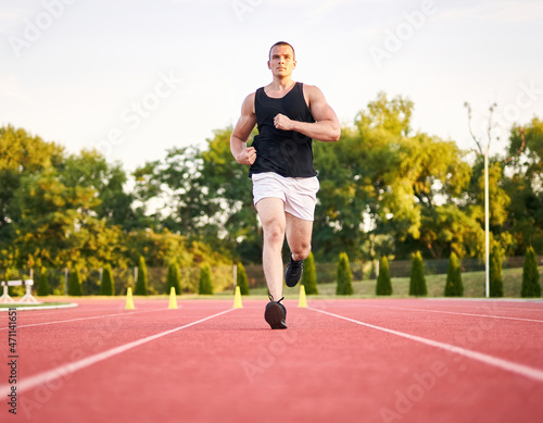 Young muscular fit male sprinter running on a red running track - Fitness and wellness concept with a millennial runner - Symmetrical, central composition