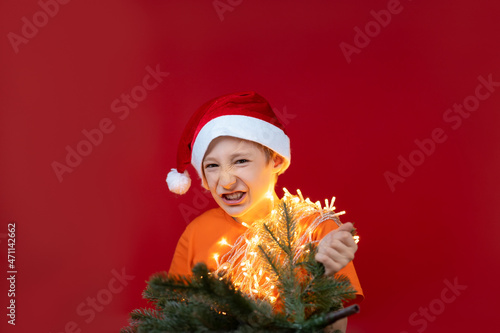 a boy in Christmas clothes is holding a Christmas tree, he grimaces and shows his teeth