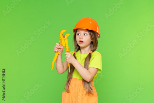 A little girl in a construction helmet looks at the wrench in surprise. Renovation and redevelopment. Construction. Isolated background. photo