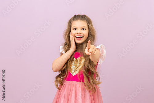 A little girl with curly hair points her finger forward. Isolated background.