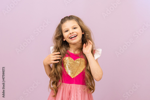 A little girl fluffs her curly, luxurious hair. Isolated pink background.
