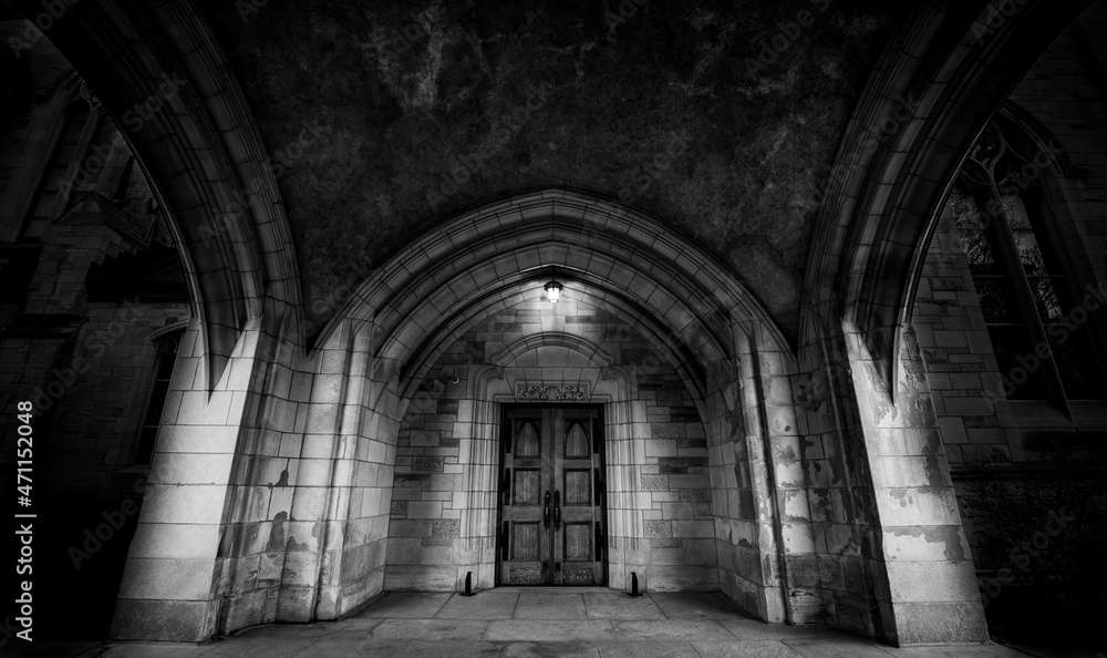 dramatic photo of the door of St. Andrew's Church in Montreal under an arched stone roof , whith a light over the door.