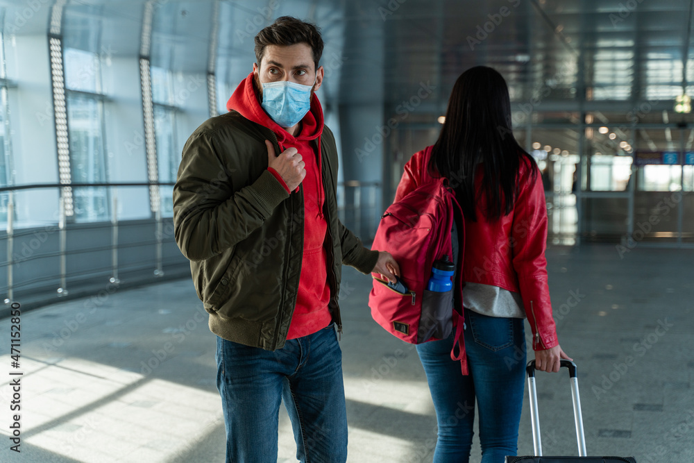 Back view of the woman with trolley bag walking through the airport while robber wearing protective mask stealing her things. Stock photo
