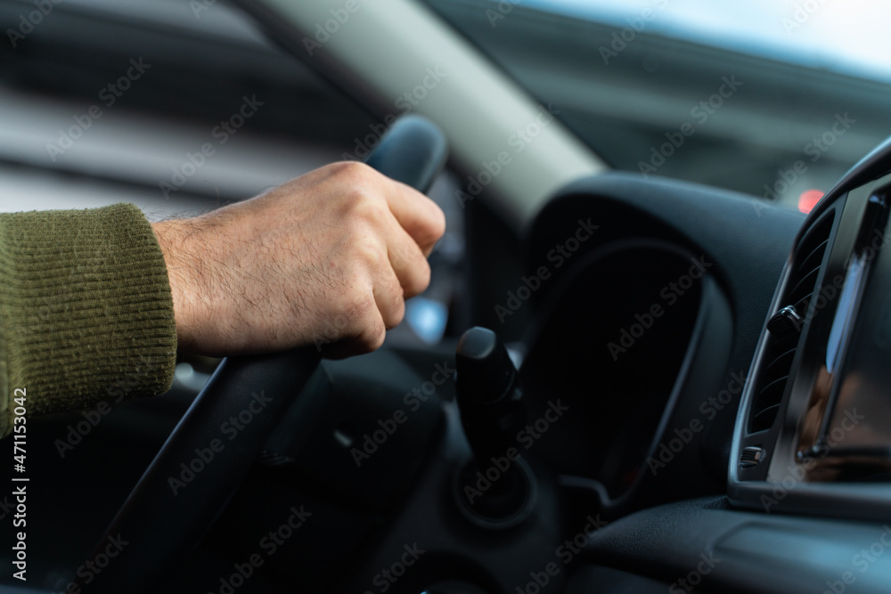 Close up of male arms holding a steering wheel. The man is sitting and driving his modern car and looking at the road. Cropped view Close up of male arms holding a steering wheel. The man is sitting and driving his modern car and looking at the road. Cropped view