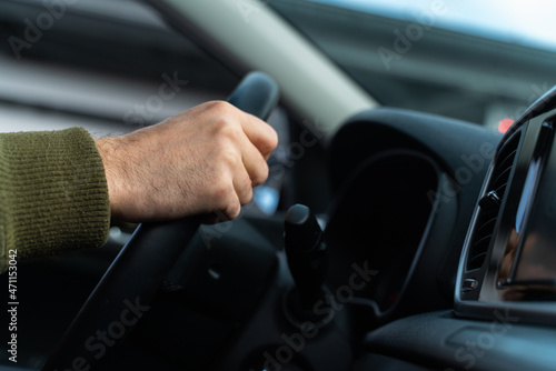Close up of male arms holding a steering wheel. The man is sitting and driving his modern car and looking at the road. Cropped view