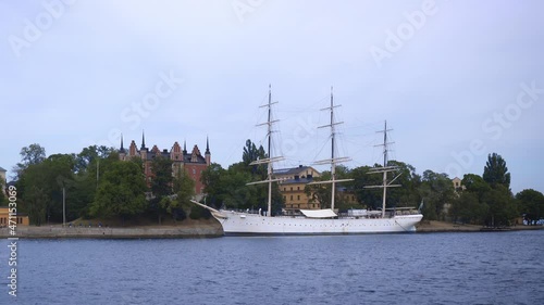 Old wooden sailboat with three masts is moored at the Stockholm embankment. Hotel ship. Skeppsholmen island connected with Blasieholmen and Kastellholmen by bridges. Panorama of the Swedish capital.