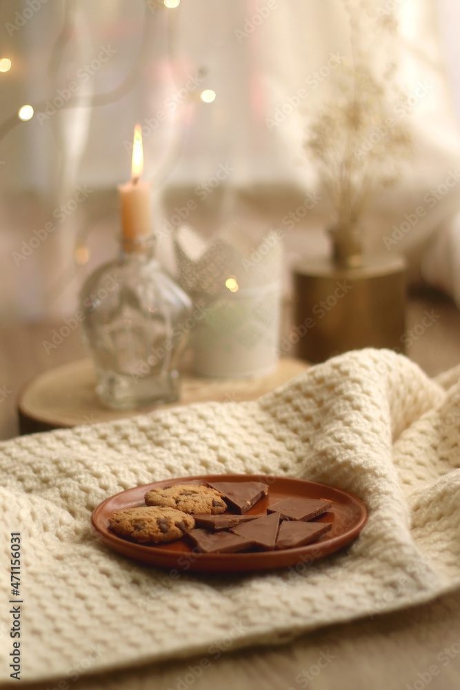 Plate of chocolate and chocolate chip cookies, knitted blanket and lit candles. Hygge at home. Selective focus. Plate of chocolate and chocolate chip cookies, knitted blanket and lit candles. Hygge at home. Selective focus.