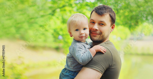 Portrait of happy father and son child on hands in summer park