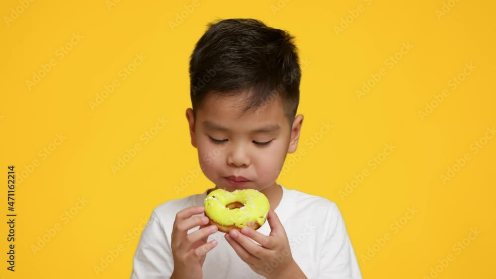 Little Asian Boy Eating Tasty Donut Standing Over Yellow Background Little Asian Boy Eating Tasty Donut Standing Over Yellow Background