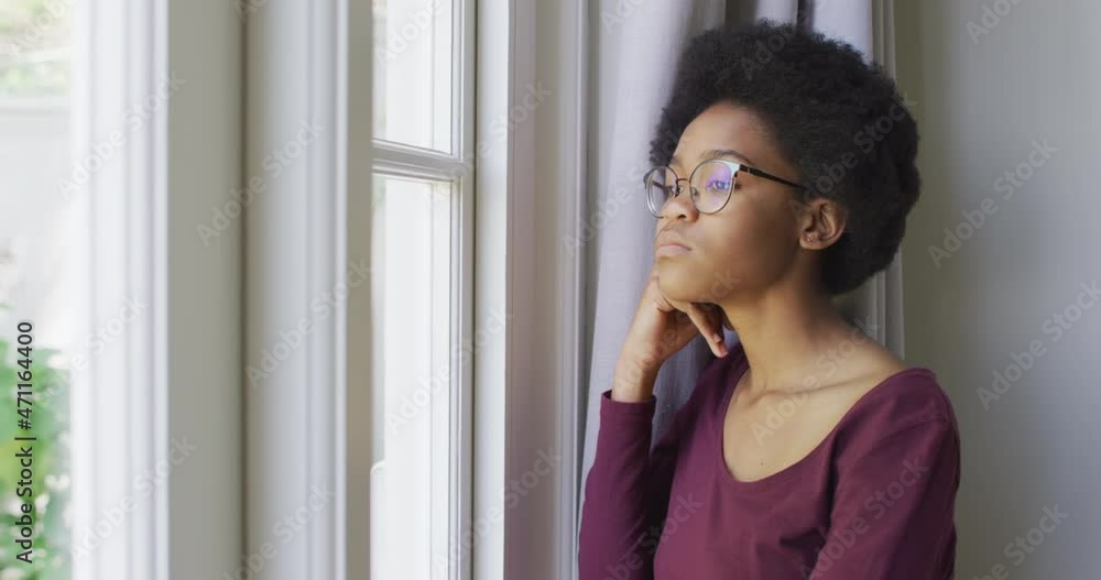 Thoughtful african american teenage girl looking through window in living room Thoughtful african american teenage girl looking through window in living room