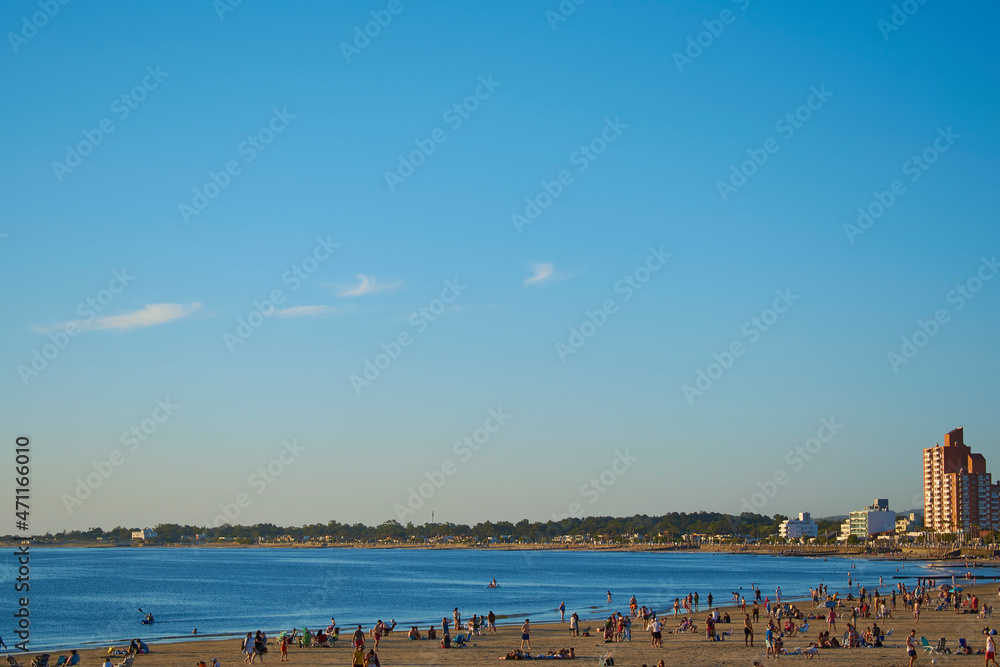 A sunny day on the beach where you can see the clear sky.
There are people on the sand enjoying the beach next to the blue sea. 