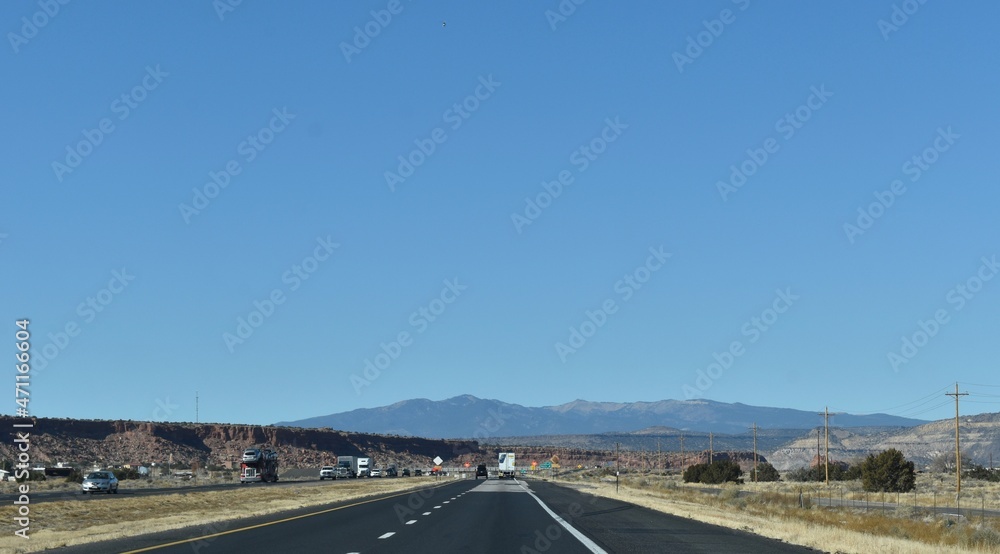 Fototapeta premium McCartys, New Mexico, USA - November 21, 2021: Mountains in the Distance as a Desert Highway Passes Through a Red Rock Valley on a Clear Fall Day