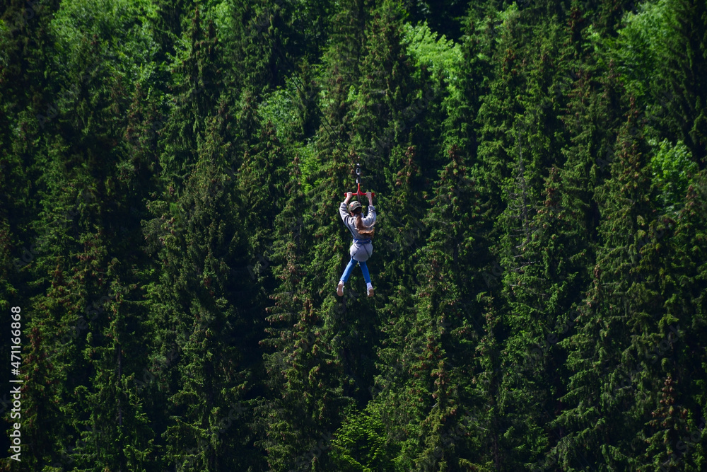A girl of unrecognizable appearance descends a tightrope on a zipline at high altitude A girl of unrecognizable appearance descends a tightrope on a zipline at high altitude