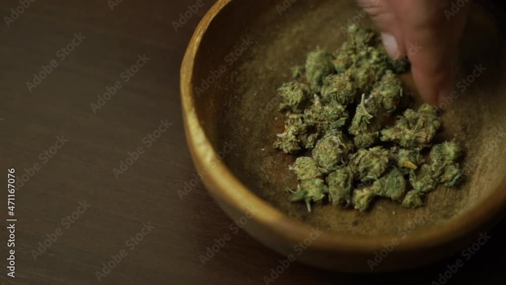 Top view cannabis buds in a wooden plate, female hand taking weed buds to smoke a joint. Decriminalization of marijuana. Legalization of medical cannabis Top view cannabis buds in a wooden plate, female hand taking weed buds to smoke a joint. Decriminalization of marijuana. Legalization of medical cannabis